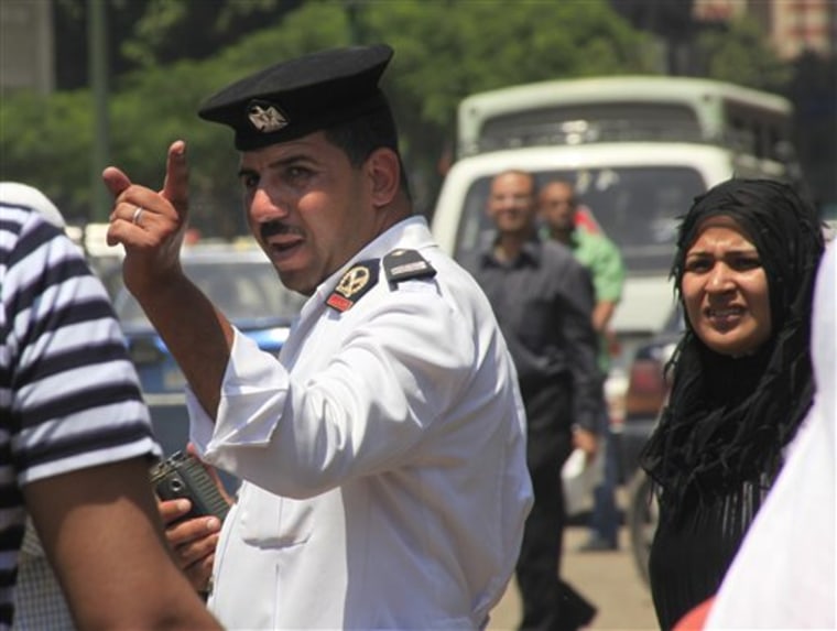 An Egyptian traffic policeman gestures Monday as he is watched by bystanders at a traffic line in Cairo, Egypt.